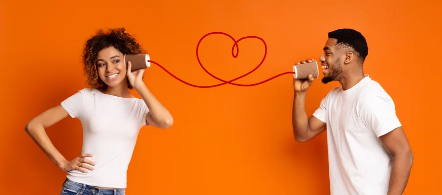 Young couple talking through a tin-can phone on an orange background